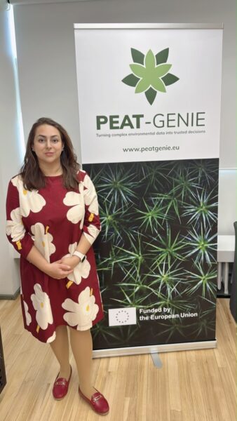 A person stands next to a PEAT-GENIE project roll-up banner.